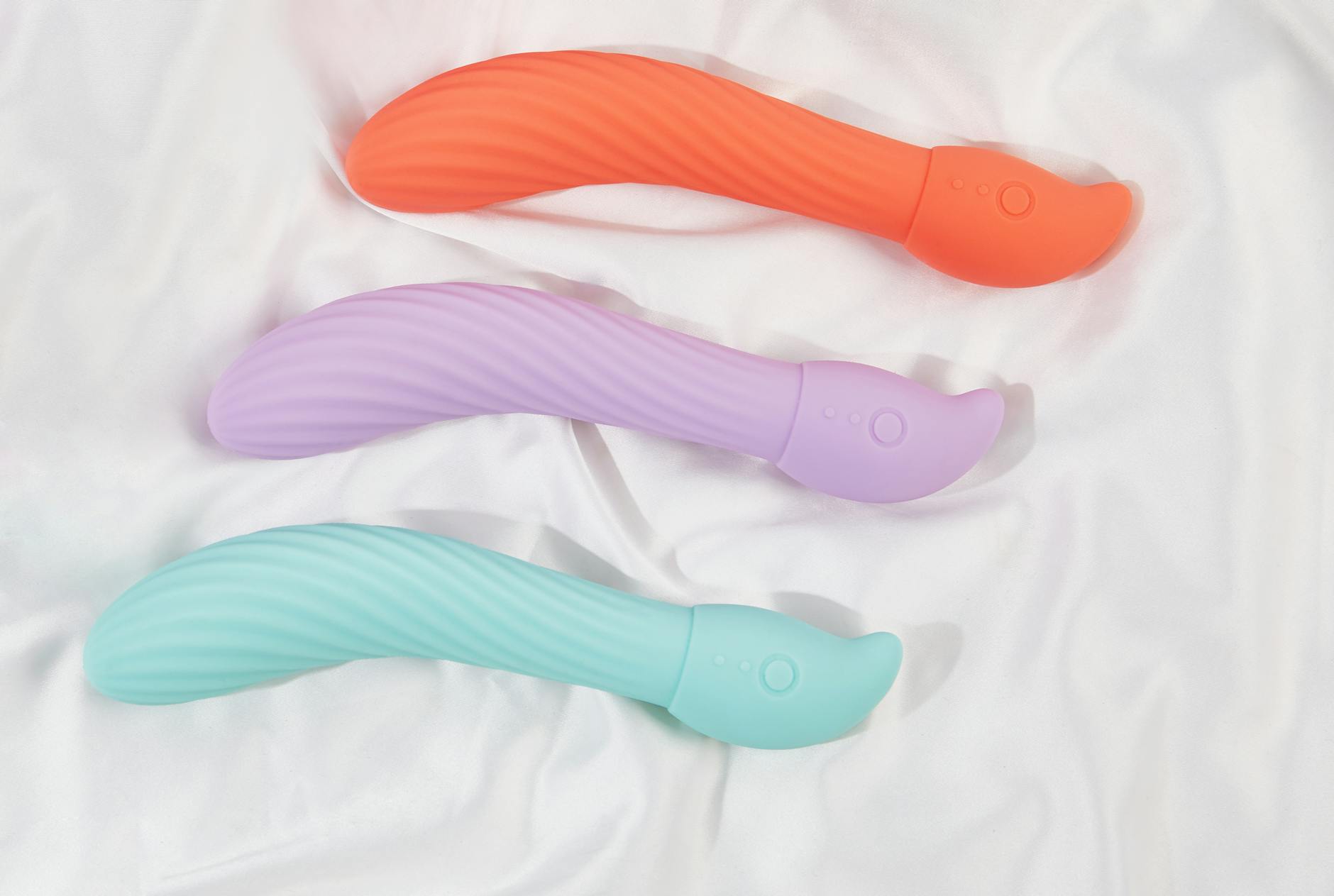 Three colorful vibrators arranged on white fabric, showing the smooth texture of suction-based clitoral stimulation tools.