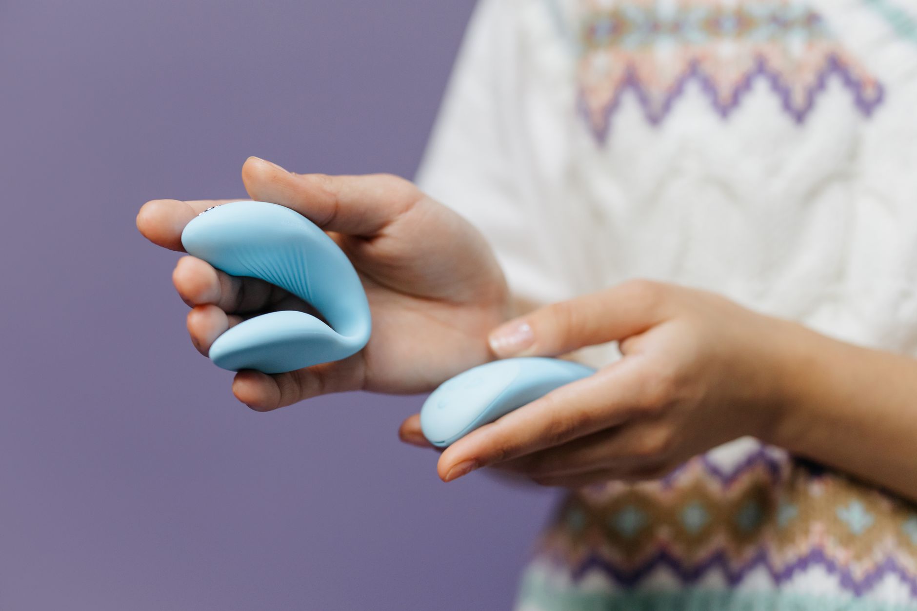 Hands holding a sleek blue lemon vibrator against a purple background